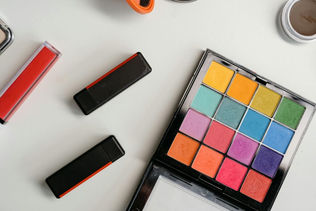 Colorful eyeshadow palette and lipstick tubes arranged in a flat lay composition.